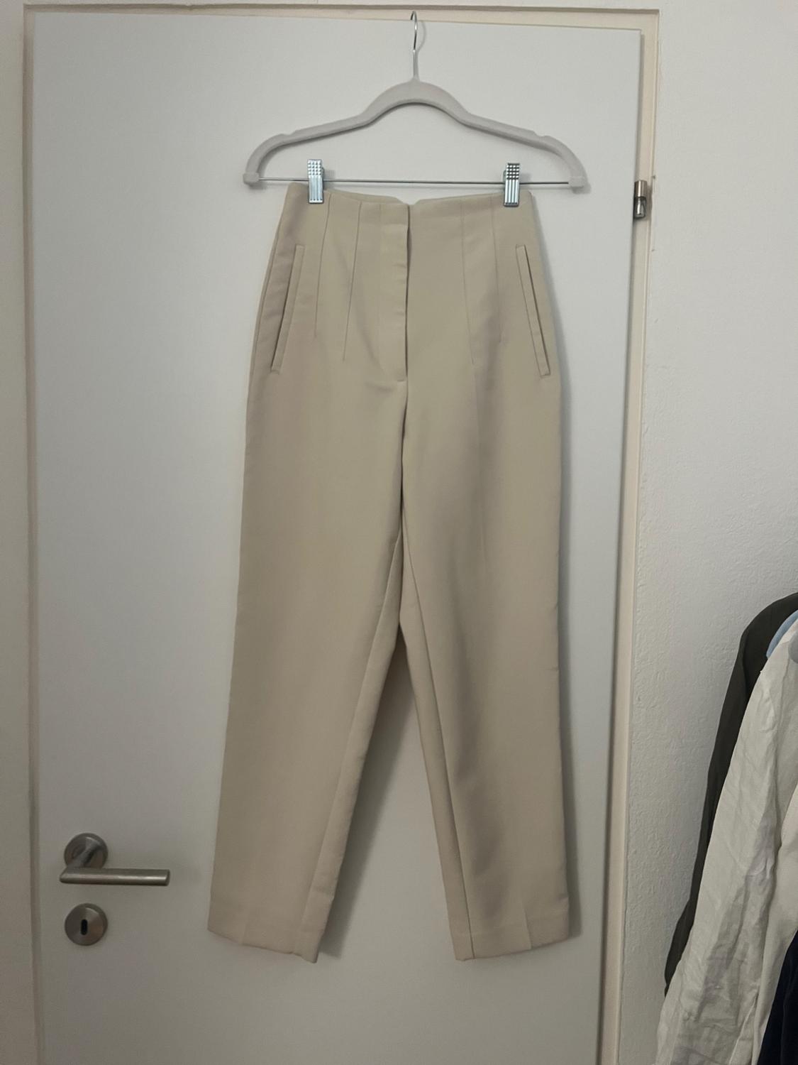 Beige trousers hanging on a hanger over a white door. To the right, part of other hanging garments can be seen.
