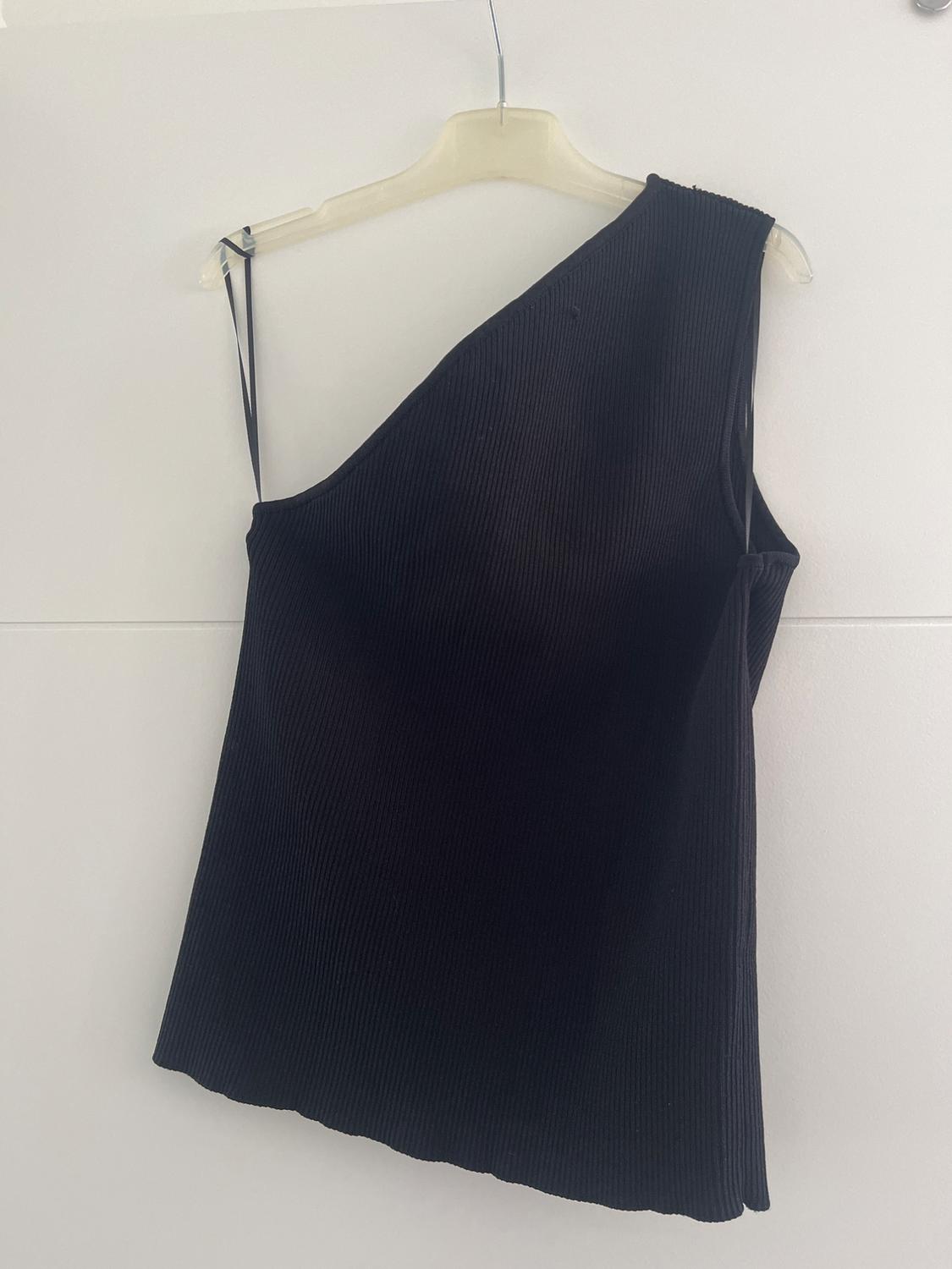 Black one-shoulder ribbed textured top, hanging on a white hanger against a white background.