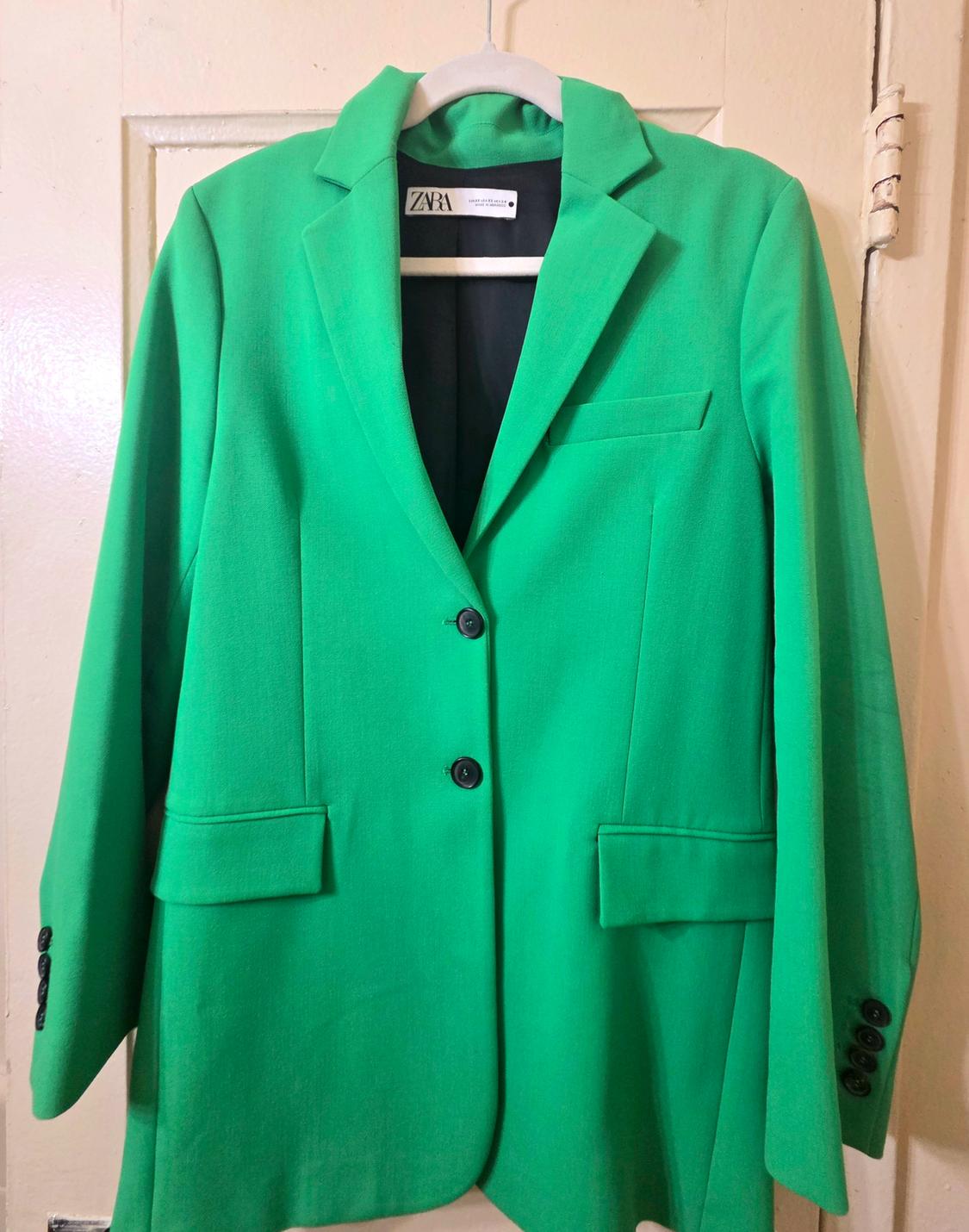 Bright green jacket hanging on a hanger, with two black buttons and front pockets. Visible label with the Zara brand.