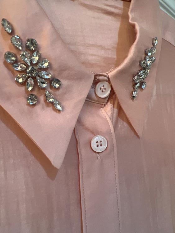 Pink satin shirt with a collar decorated with shiny rhinestones and white buttons. Soft and elegant texture detail.