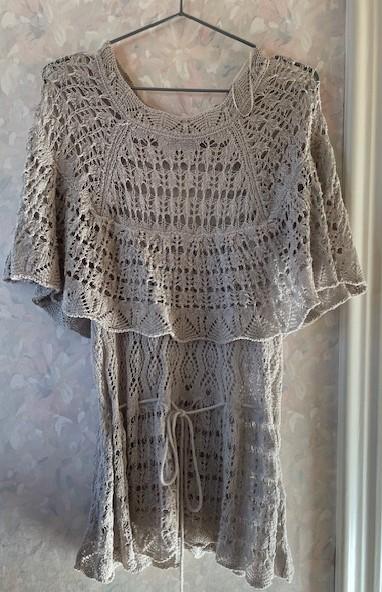 Beige lace dress hanging on a hanger against a floral wallpaper background. Ruffled design with a drawstring waist.