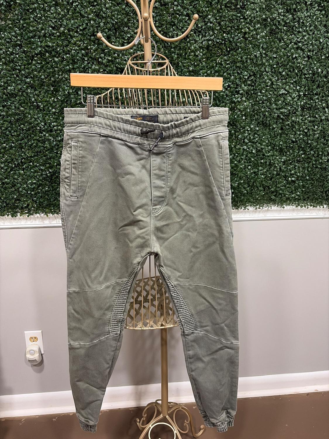 Gray jogger pants hanging on a gold clothing rack in front of a green leaf wall. On the floor, a visible outlet.