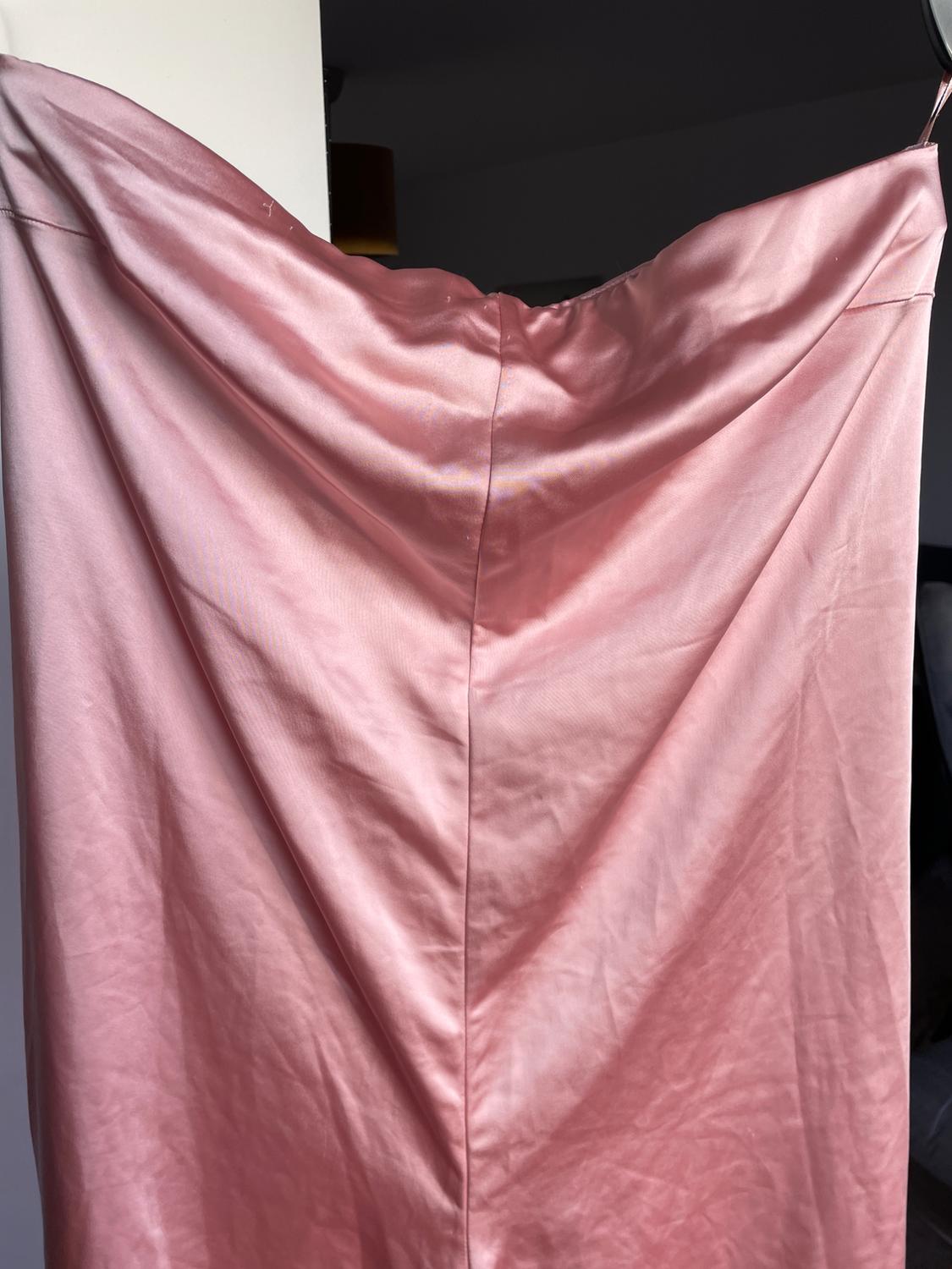 Pink satin dress hanging on a hanger, showcasing its smooth texture and fluid drape in an indoor setting.