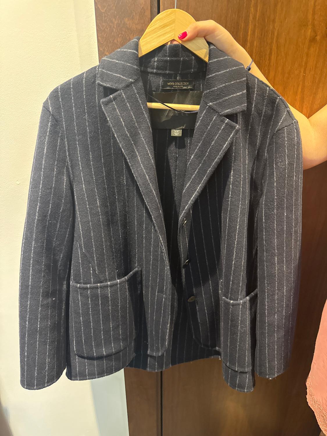 A jacket with vertical stripes in dark tones is hanging on a wooden hanger, held by a hand with red painted nails.