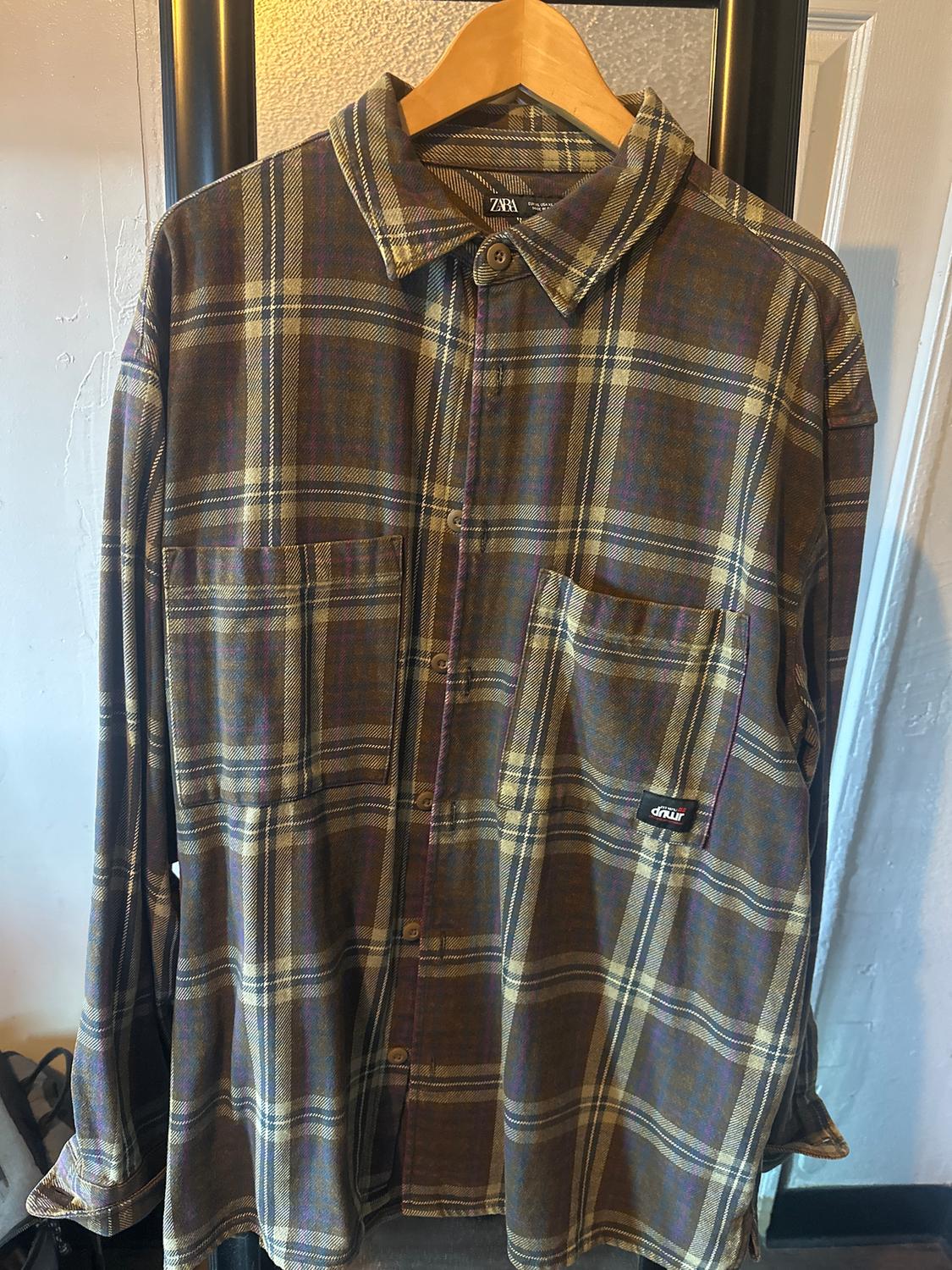 Brown and beige checked shirt hanging on a wooden hanger. Visible "ZARA" label on the collar.