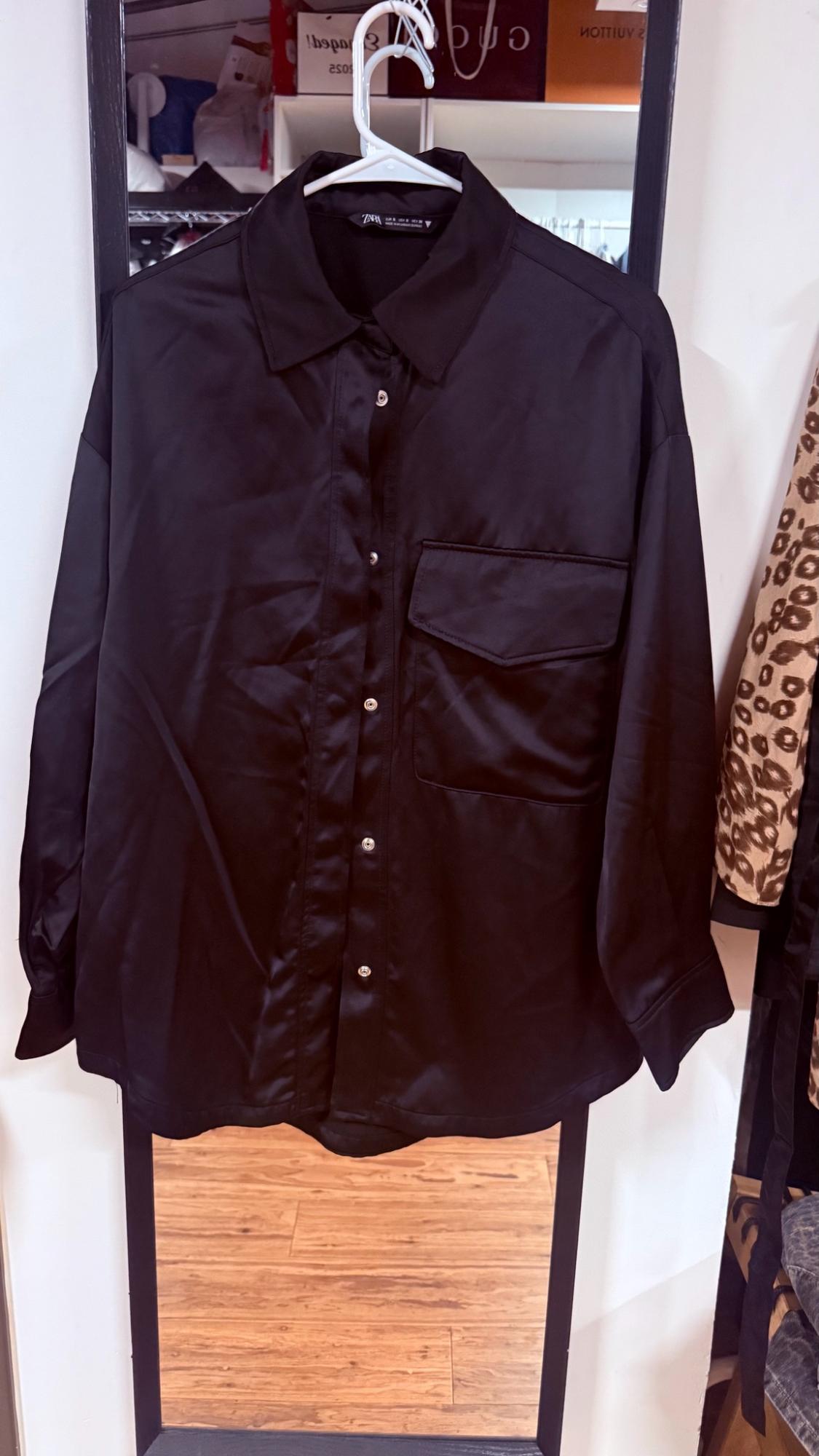 Black long-sleeve button-down shirt with a chest pocket and ZARA label, hanging on a hanger in front of a mirror.