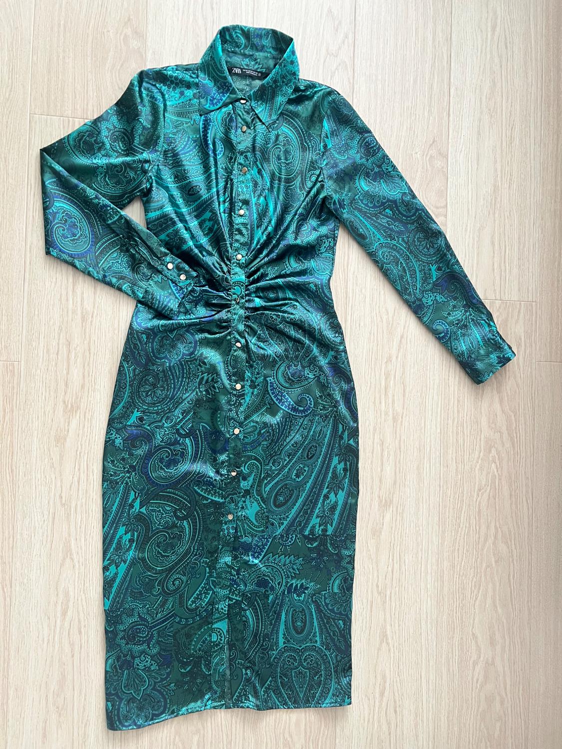 Green dress with paisley print, long sleeves, and front buttons, on a light wooden floor.
