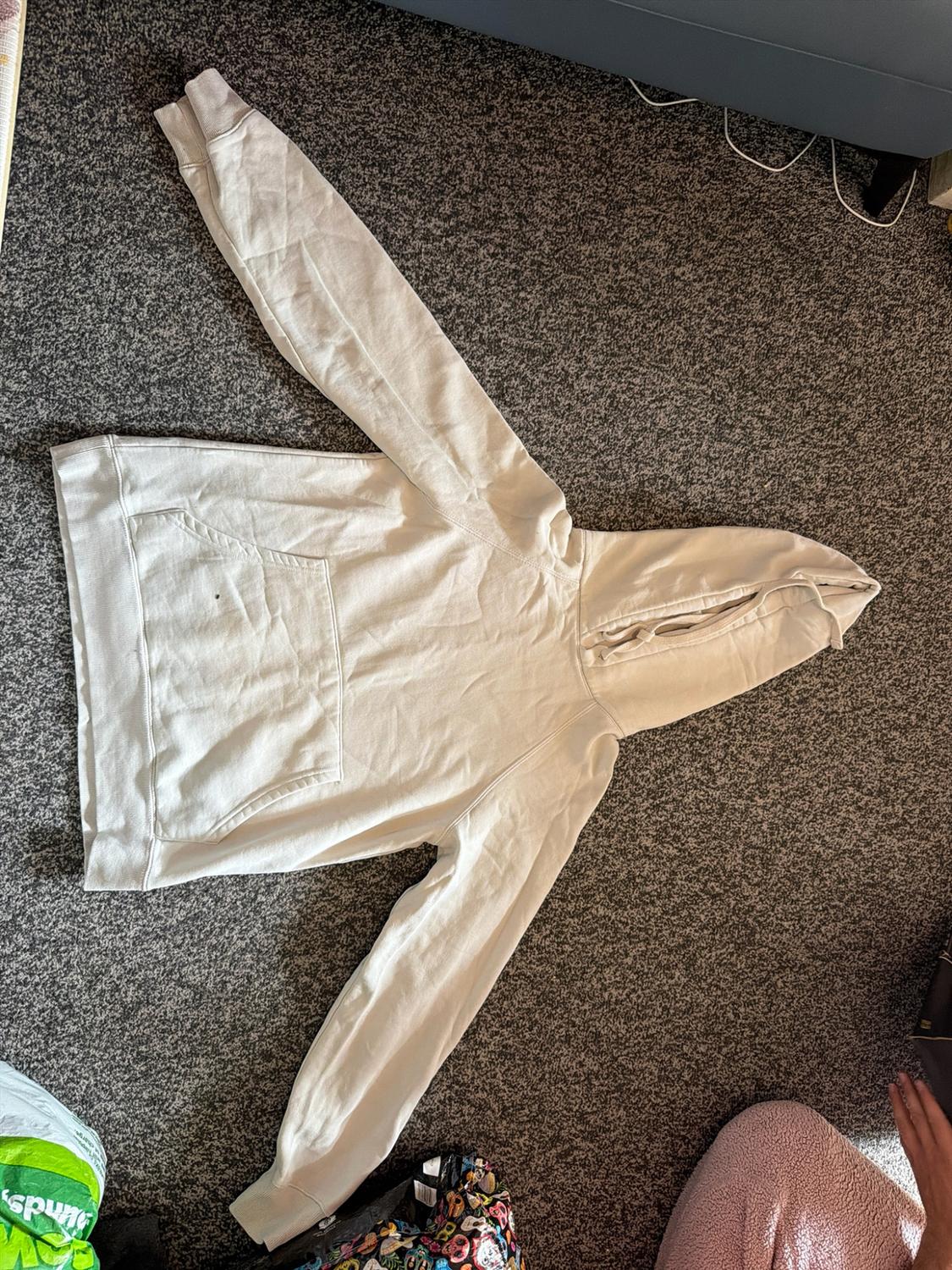 White hooded sweatshirt with a front pocket laid out on a grey carpet in a relaxed home setting.