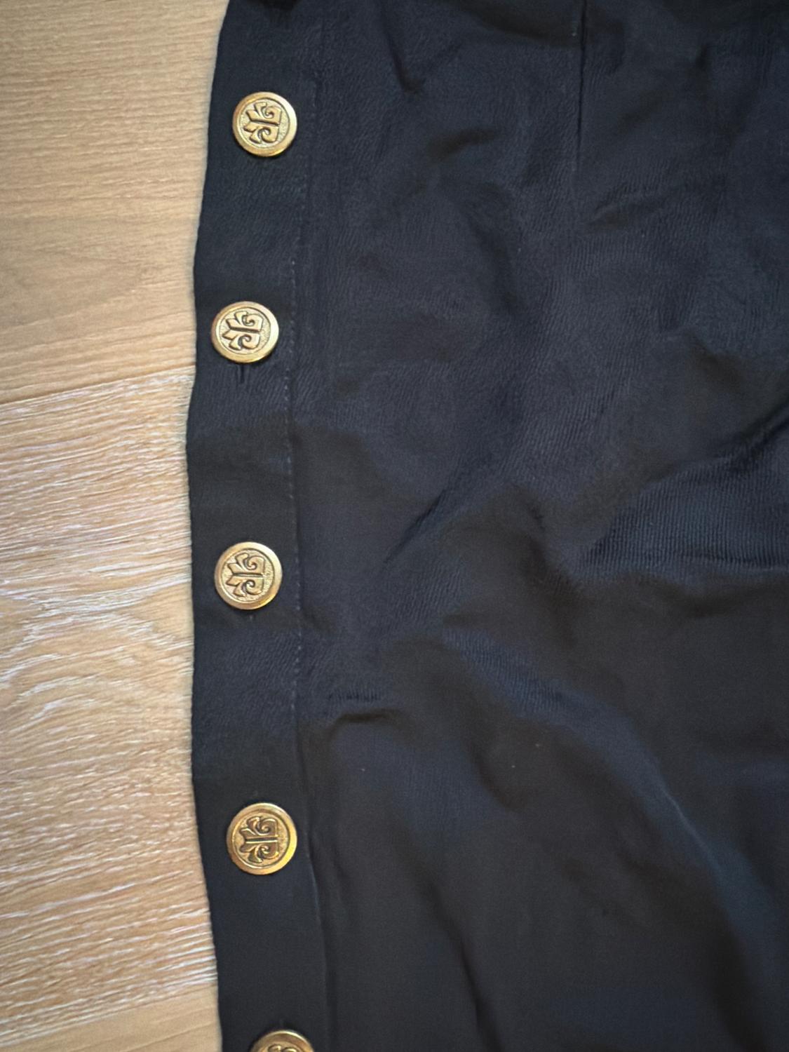 Black fabric with decorative gold buttons in a vertical row on a light wood background.