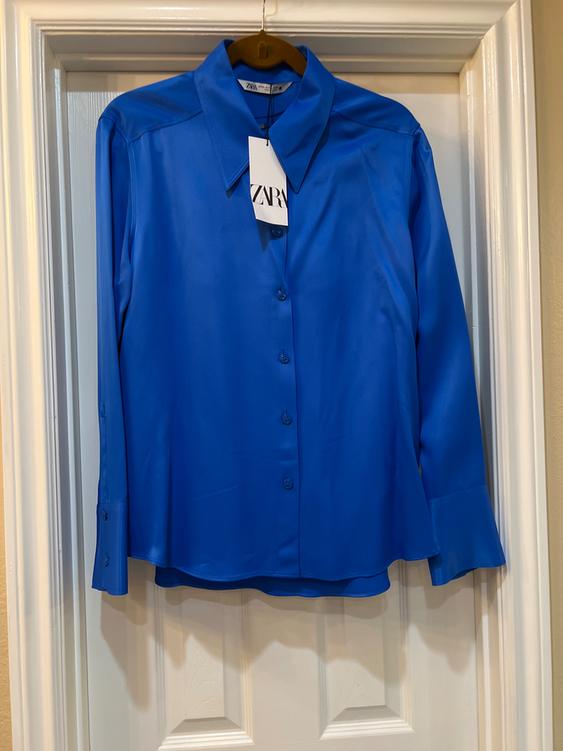 Blue long-sleeved shirt hanging on a white door, with a visible tag that says "ZARA".