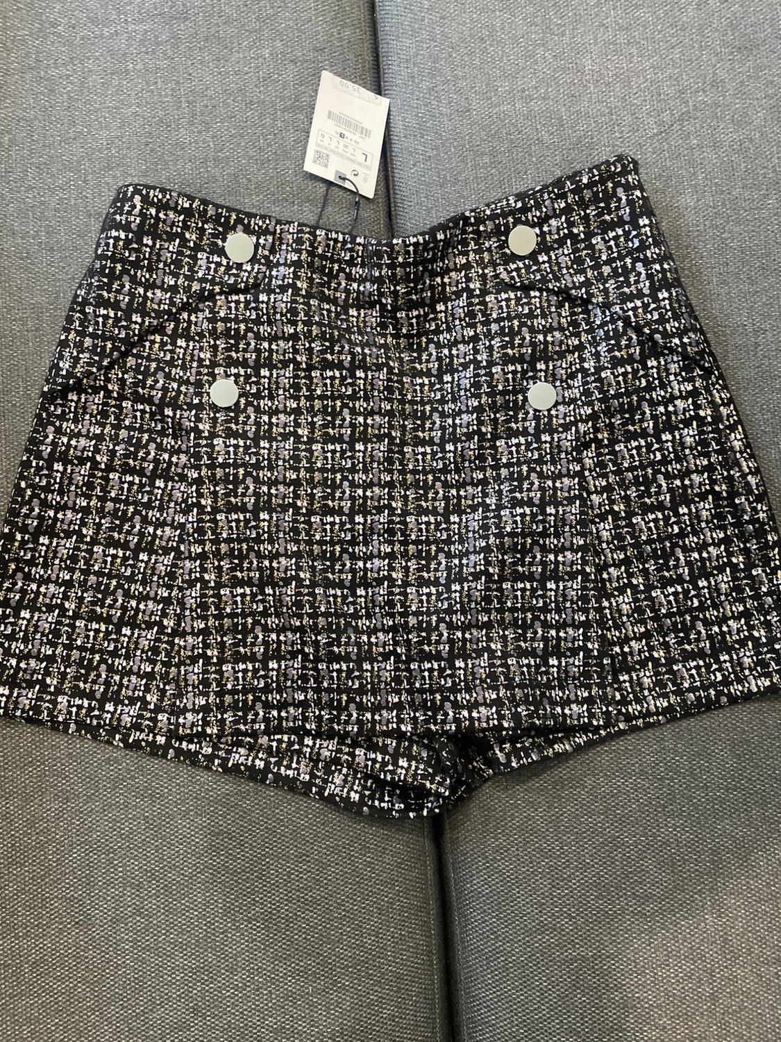 Black and white textured mini skirt with silver buttons, on a grey sofa. Visible tag at the top.