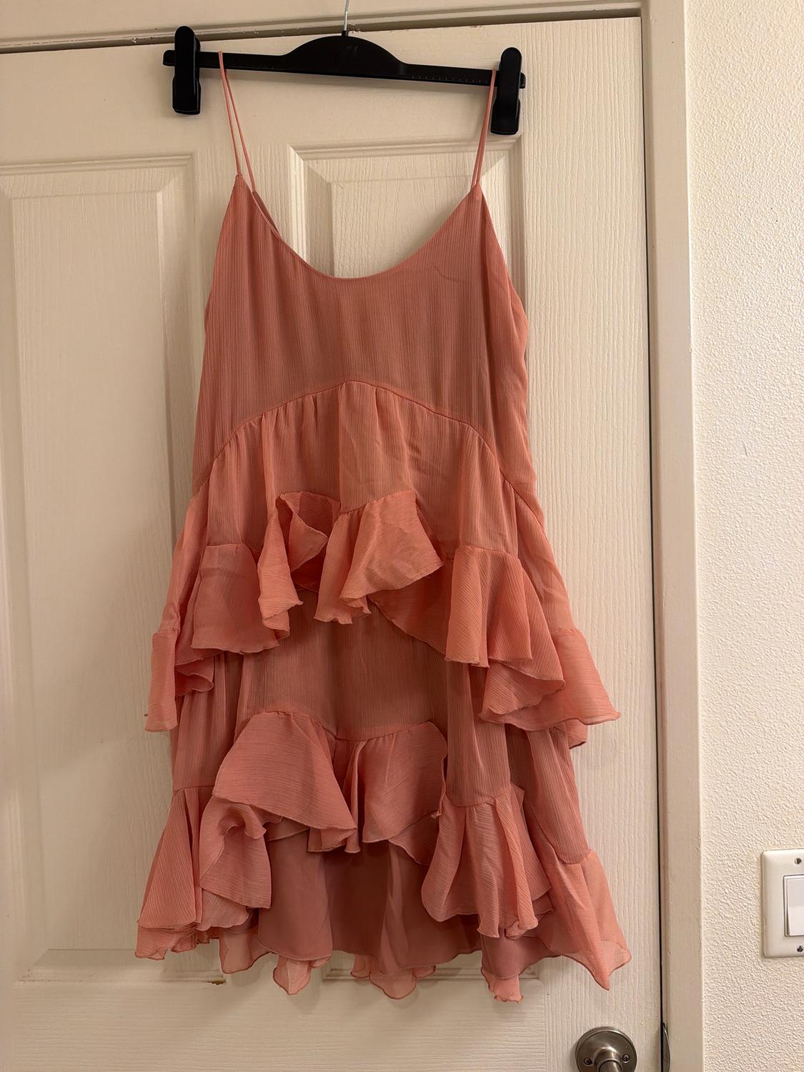 Pink dress with thin straps and layered ruffles, hanging on a black hanger over a white door.