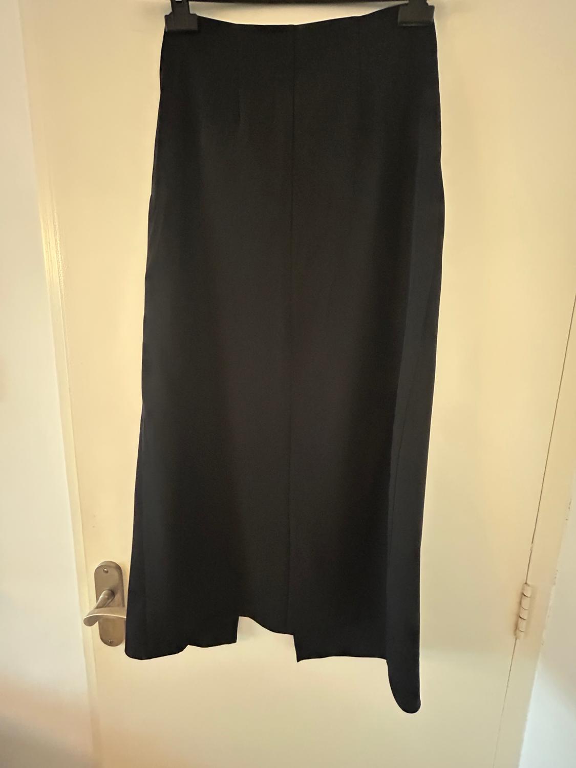 Long black skirt hanging on a white door, with a simple and elegant design. The door has a silver handle.