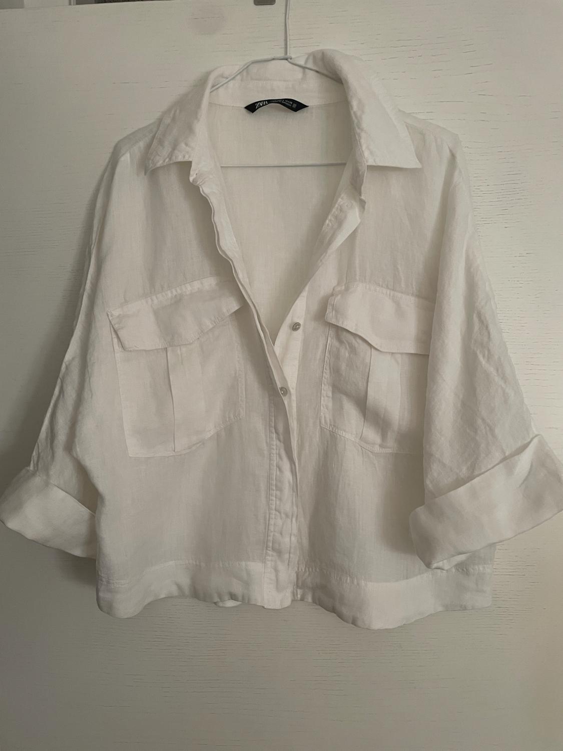 White button-up shirt, two front pockets and rolled-up sleeves, hanging on a hanger over a white door.