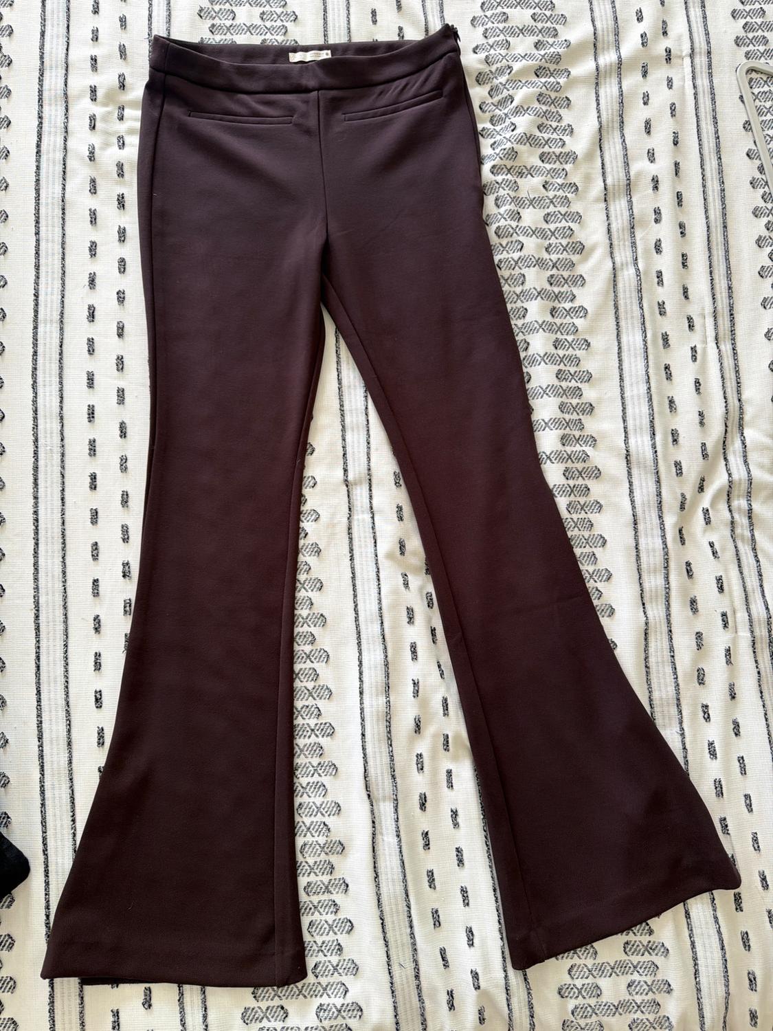 Dark brown flared trousers laid out on a white fabric with black stripes. Relaxed and casual composition.