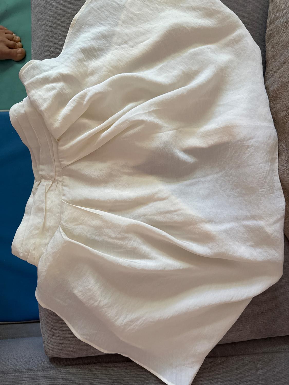 White lightweight fabric skirt on a gray sofa, with a blue and gray background. Part of a foot visible in the upper left corner.