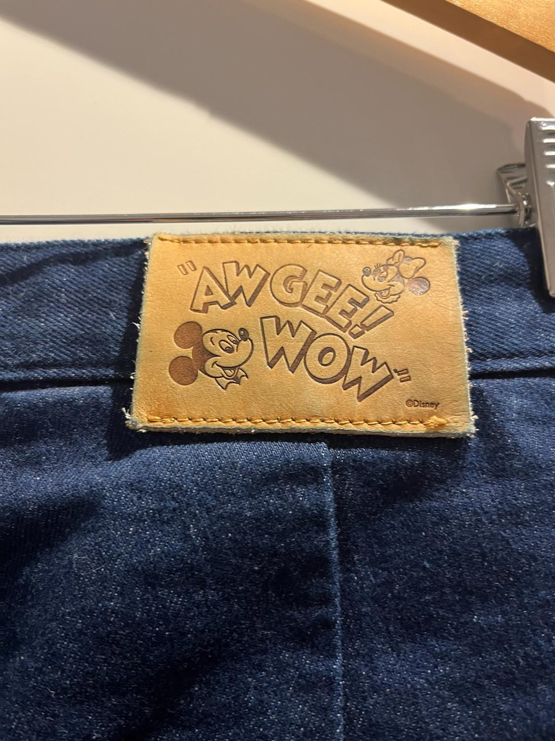 Λεπτομέρεια από μπλε τζιν με δερμάτινο patch. Εμφανίζει το κείμενο «AW GEE! WOW», πρόσωπα του Μίκυ και της Μίνι Μάους και την ένδειξη «©Disney».
