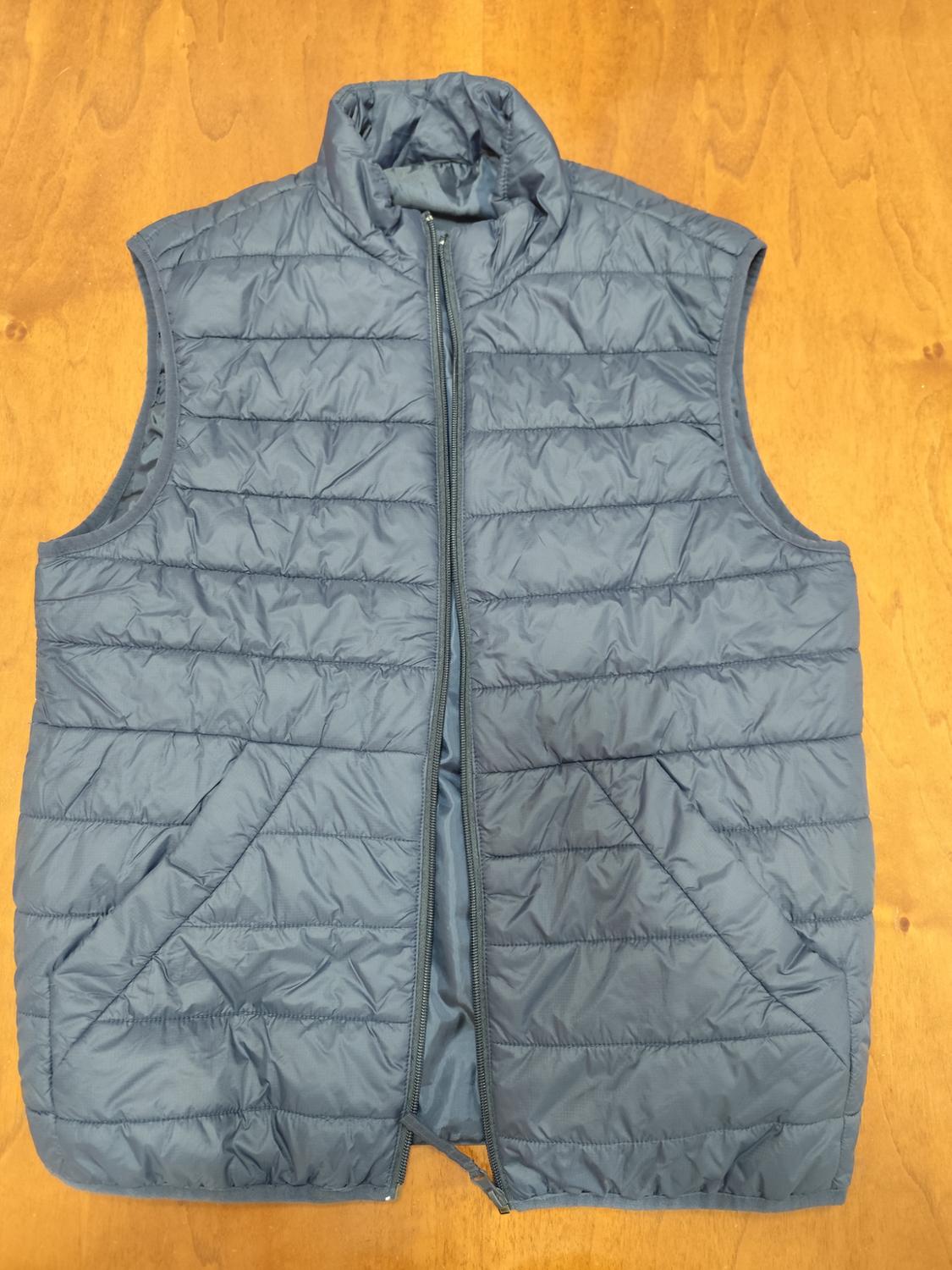 Grey padded gilet with front zip, sleeveless, on a light wood background.