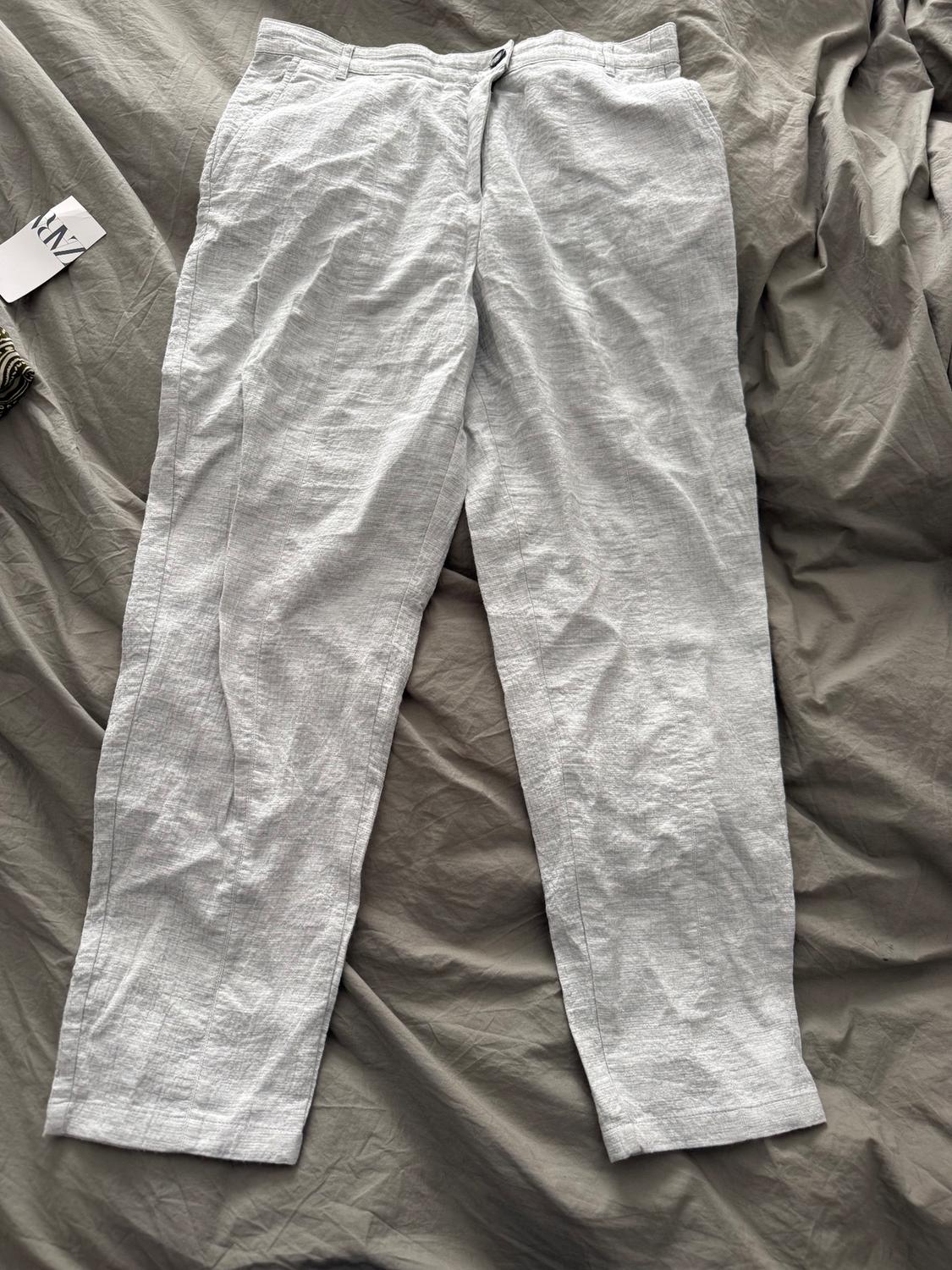 Wrinkled gray linen pants on a gray fabric. Label visible on the left with text "ZARA".
