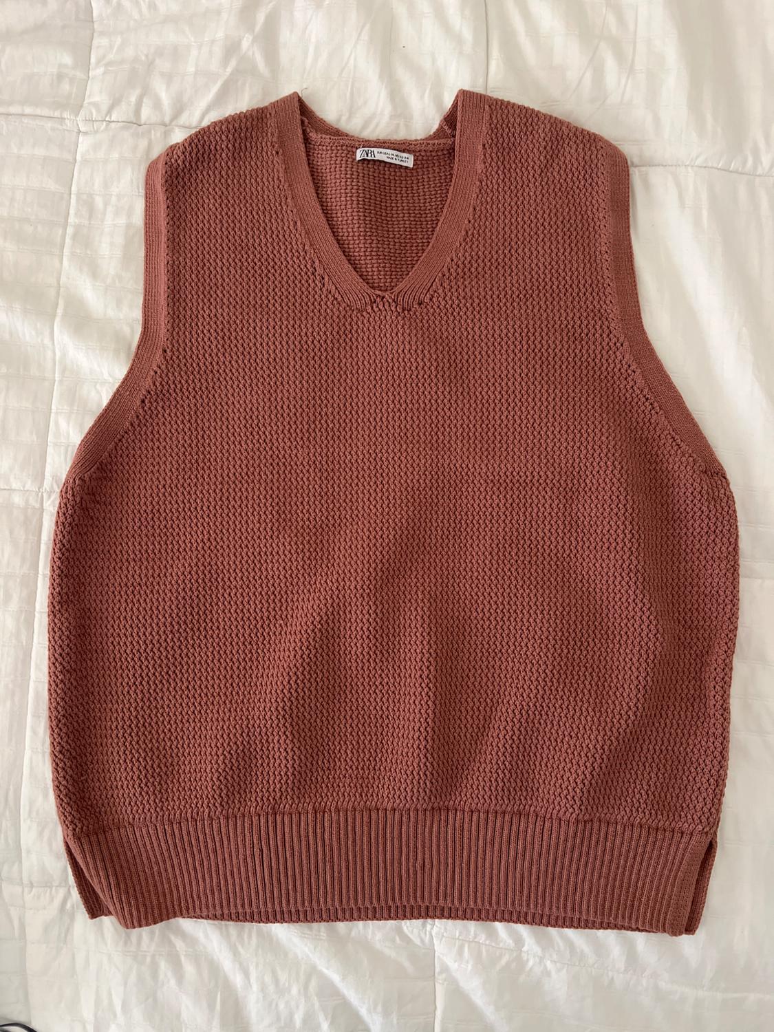 Brick-colored knit vest with a V-neck and ribbed hem, laid out on a white sheet. ZARA label visible at the neckline.