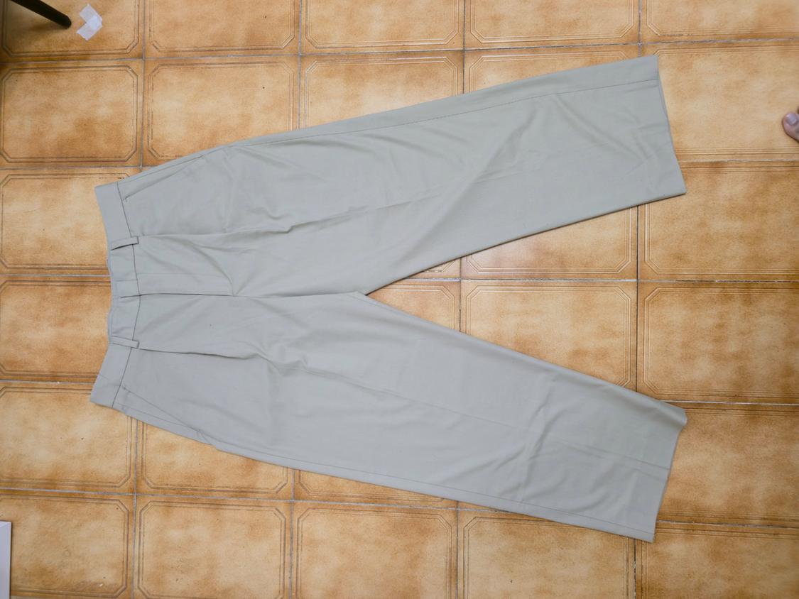 Straight-cut beige trousers laid on a brown tiled floor.
