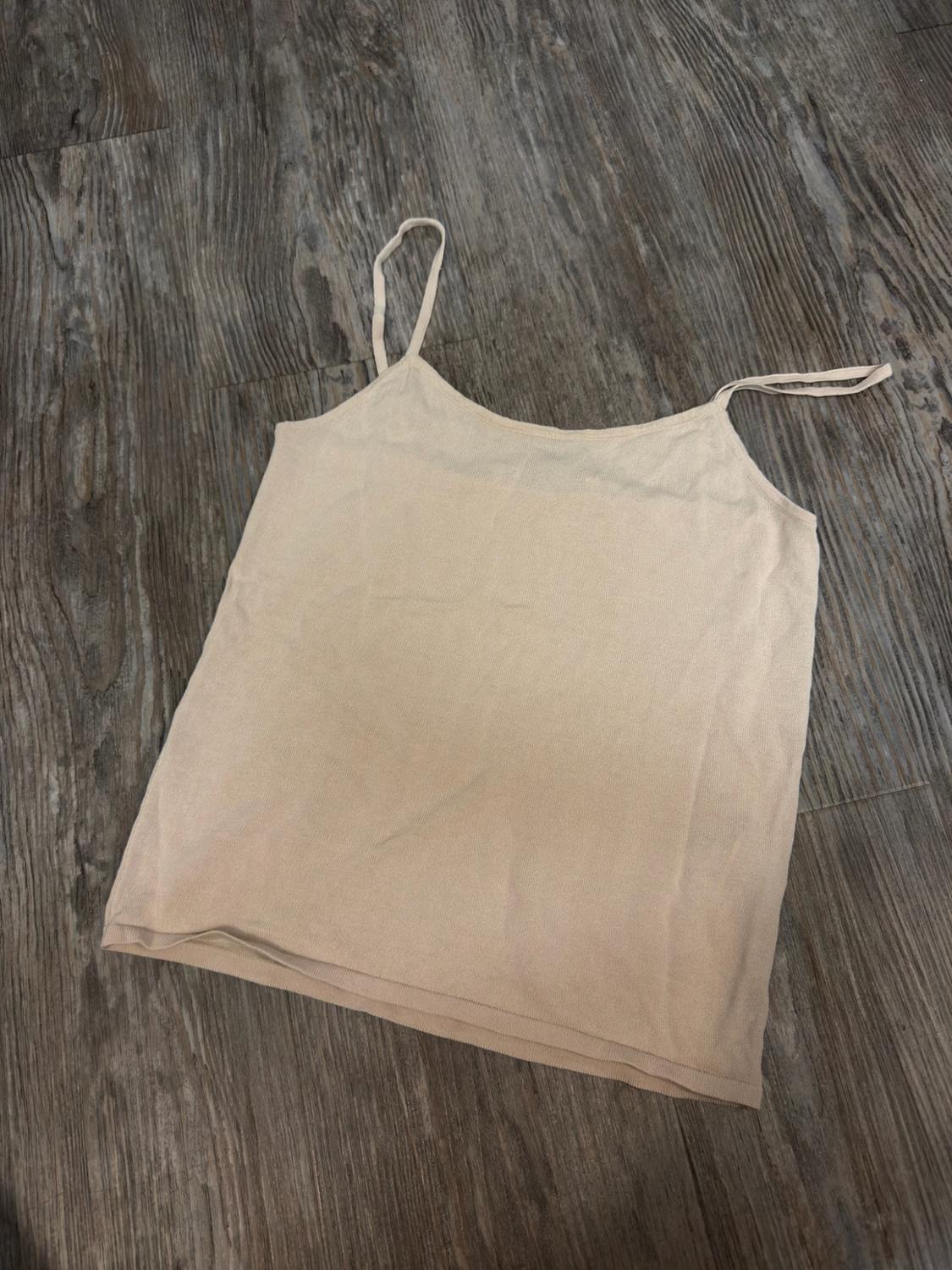 Basic camisole top with thin straps in light beige, laid flat on a rustic wooden floor with visible grain.
