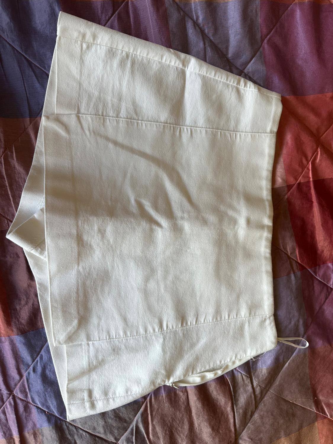 White culottes with a side zip, on a purple and reddish geometric print bedspread.