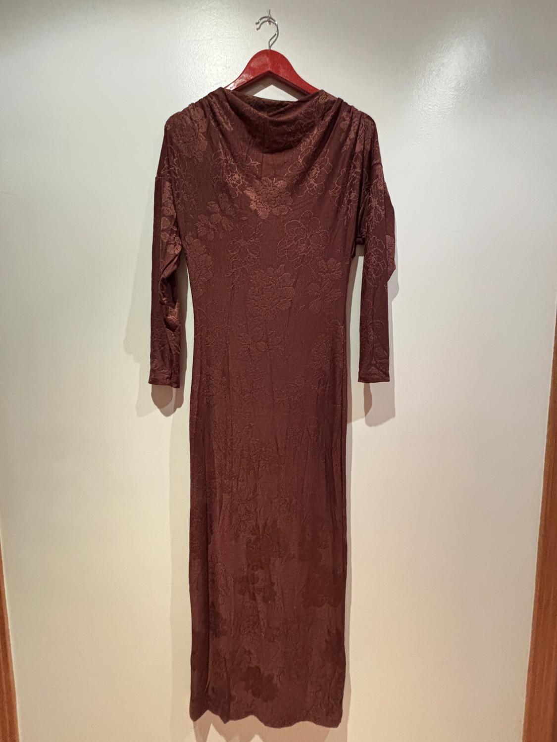 Long-sleeved brown maxi dress with a floral pattern, hanging on a red hanger in front of a white wall.
