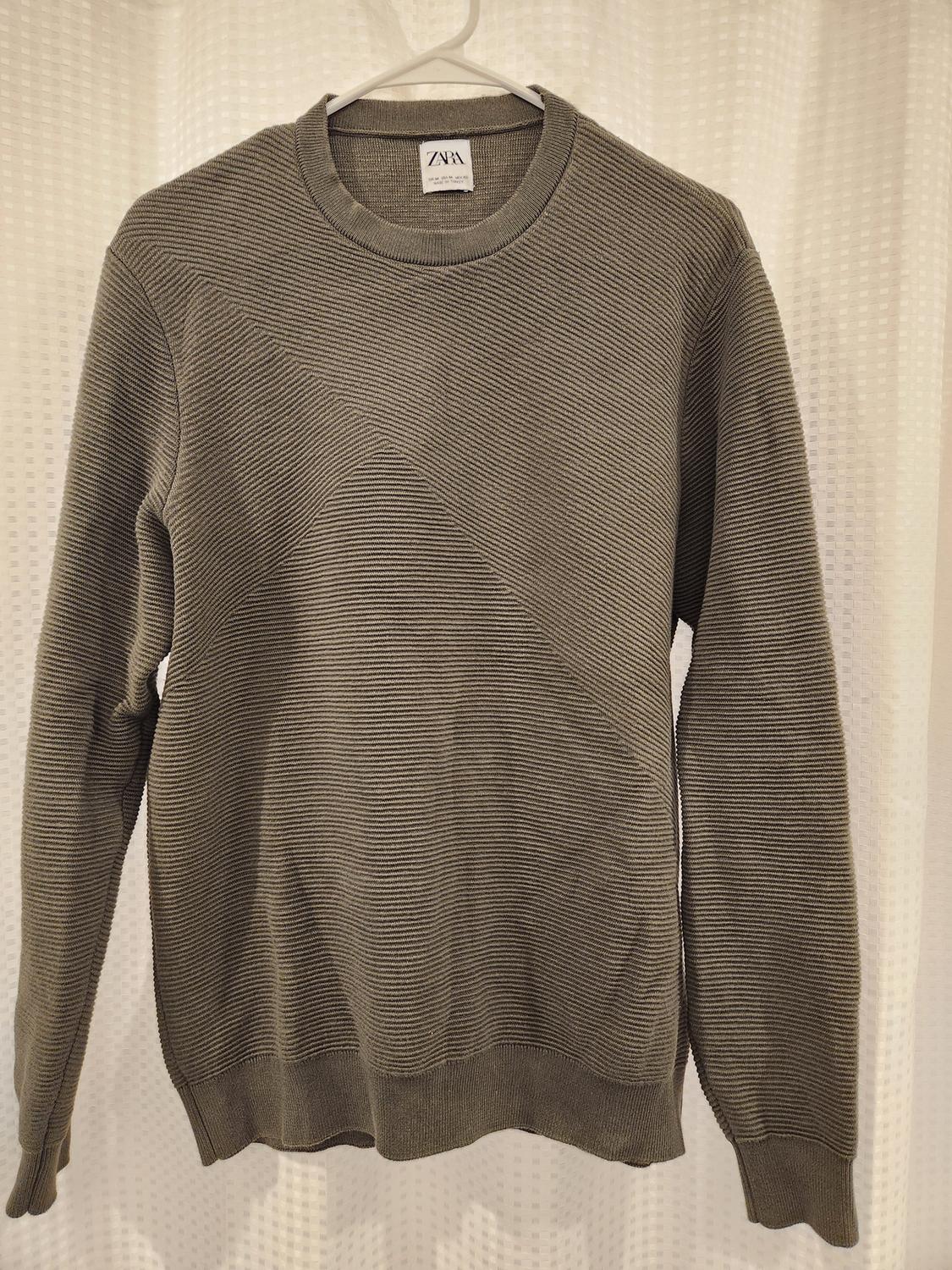 Textured gray sweater hanging on a white hanger, with a visible tag that says "ZARA". White curtain background.