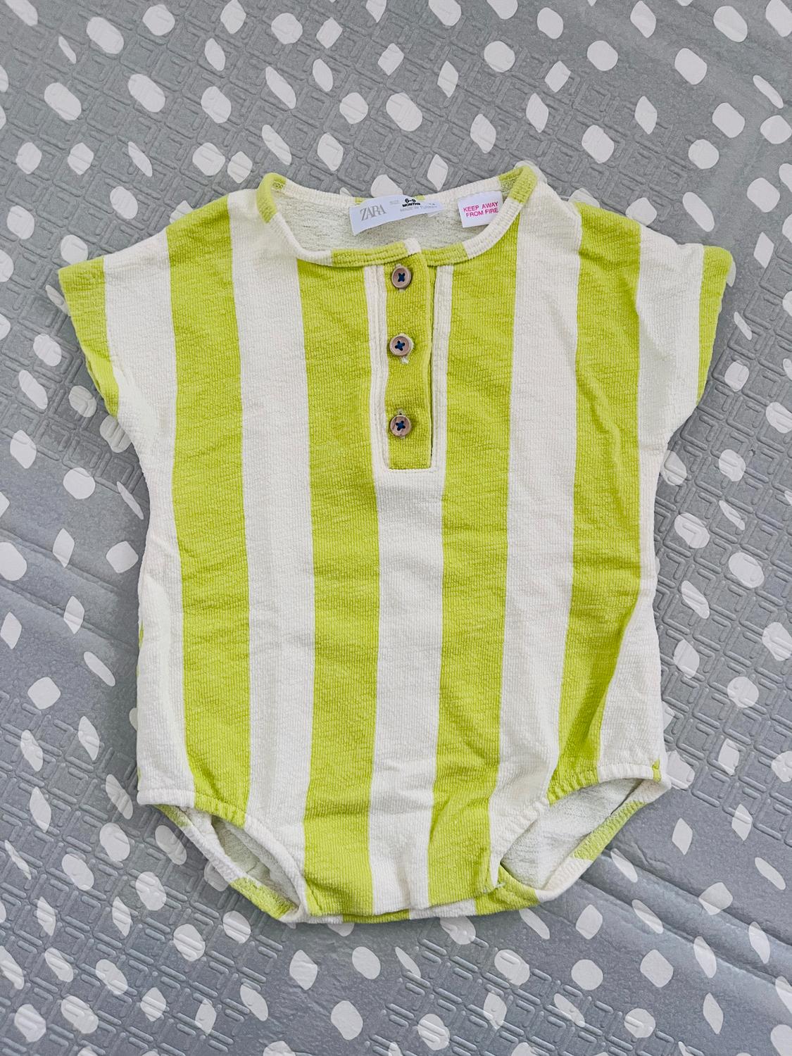 Green and white striped babygrow with buttons on the front, on a grey quilt with a dot and diamond pattern.