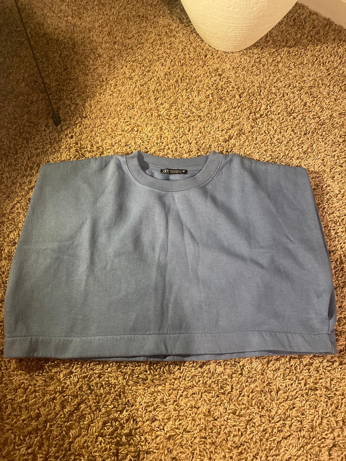 Blue t-shirt folded on a brown rug, with a visible label on the collar. Warm and cosy atmosphere.