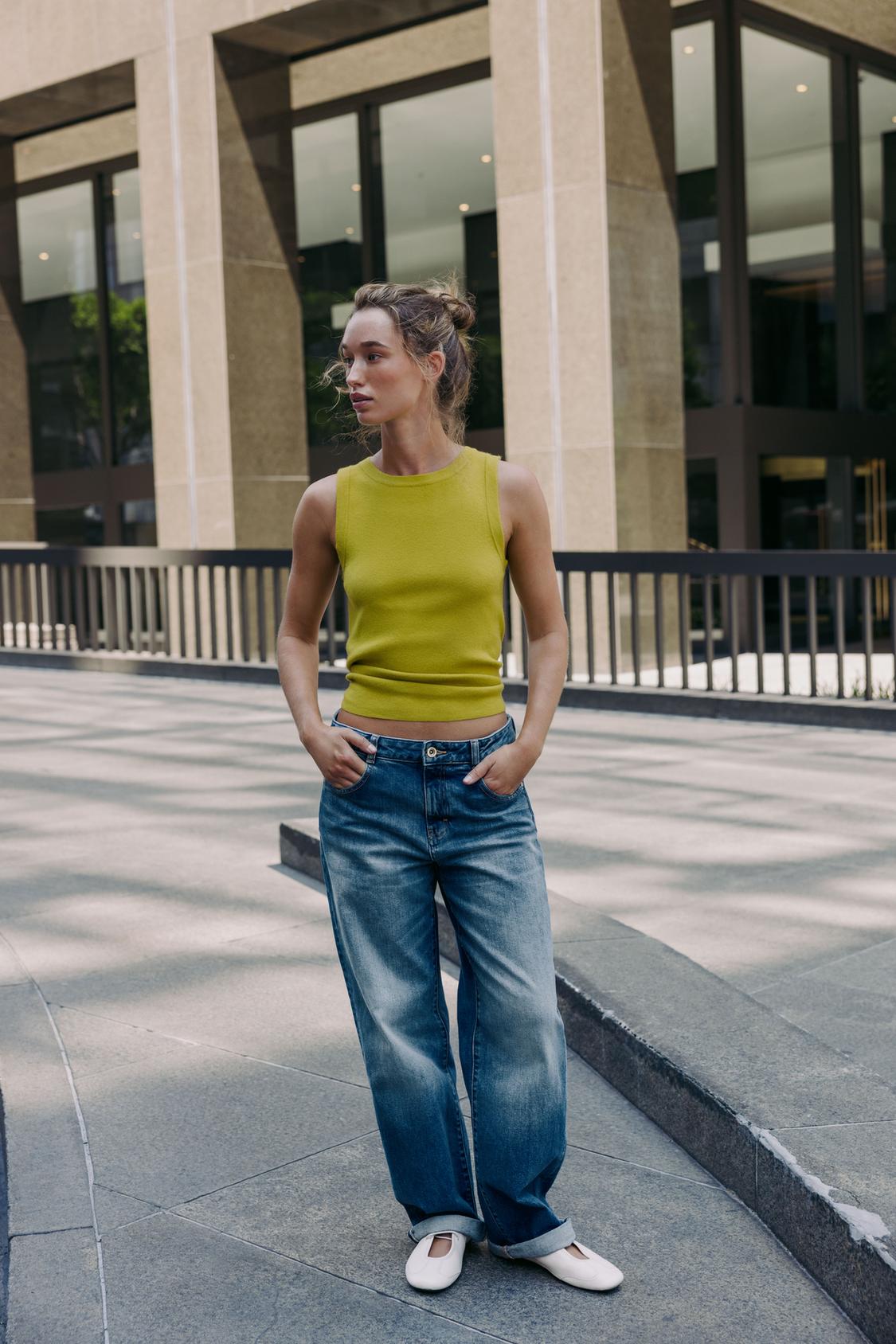 Komplet rumenega brezrokavnega topa in modrih jeans ravnega kroja z zavihkom, brez vidnih žepov.