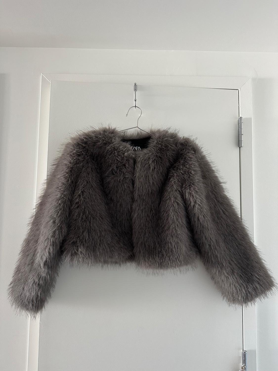 Gray fur jacket hanging on a hanger over a white door. Minimalist and modern atmosphere.