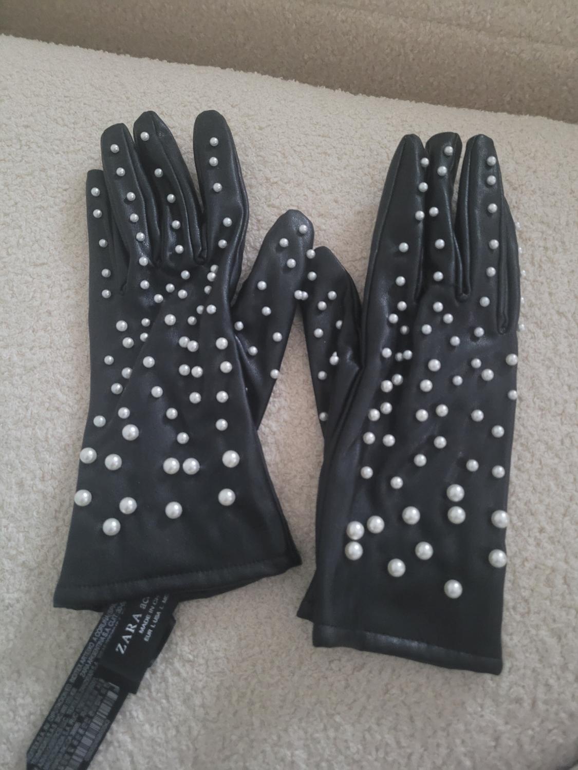 Black gloves with white pearls on a beige surface. Visible label with text "ZARA A.G.".