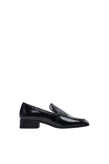 Black patent leather shoe with low heel and elegant design on a white background.
