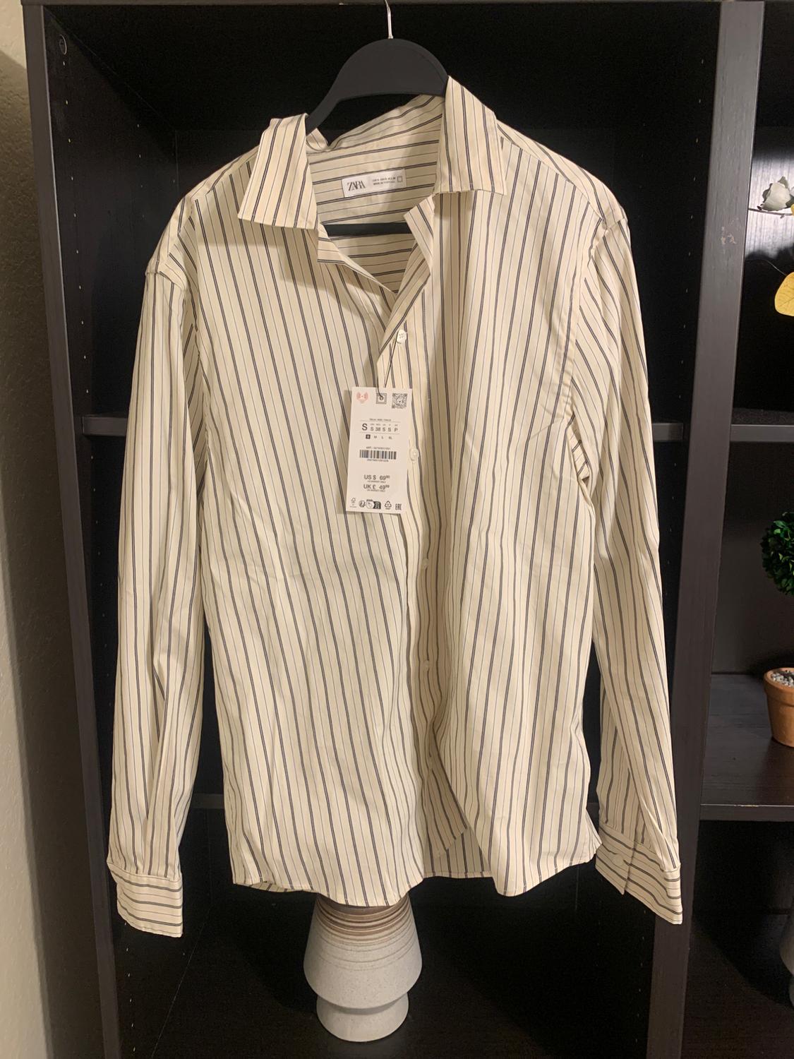 Black and white vertical striped shirt hanging on a black hanger, with visible price tag, against a shelving background.