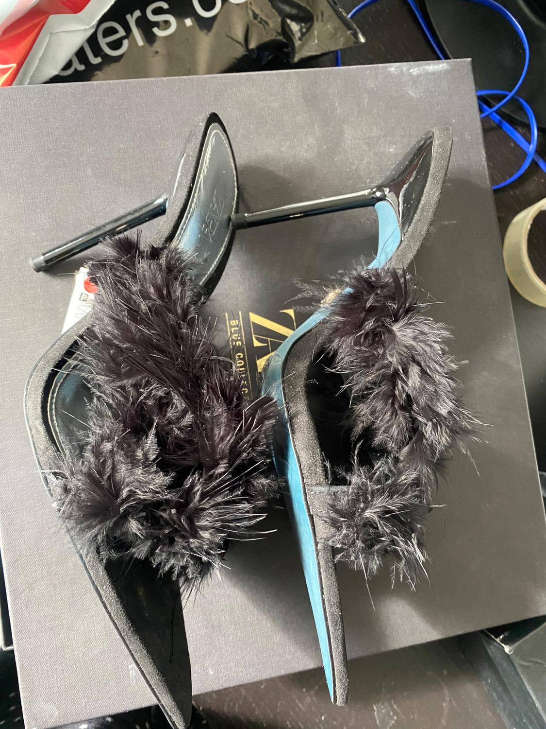 Black high-heeled shoes with feather details on a cardboard box.