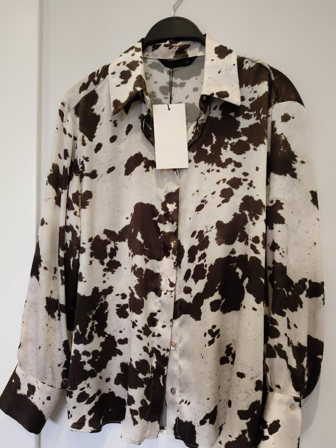 Long-sleeved shirt with brown and white spot print, hanging on a black hanger. Label visible on the collar.