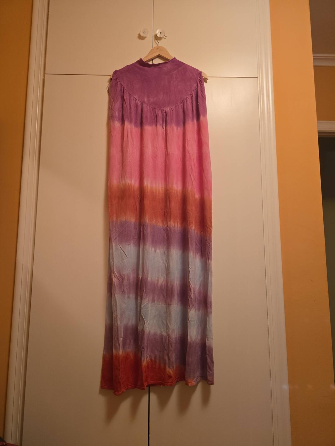 Long high-neck dress with horizontal stripes fading from purple to pink, orange and blue, hanging in a white wardrobe.