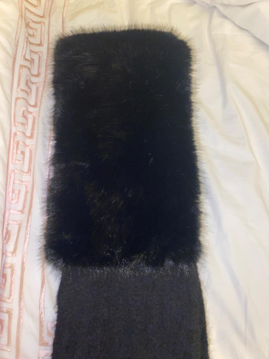 Black faux fur scarf on a bed with a white quilt and pink geometric details.