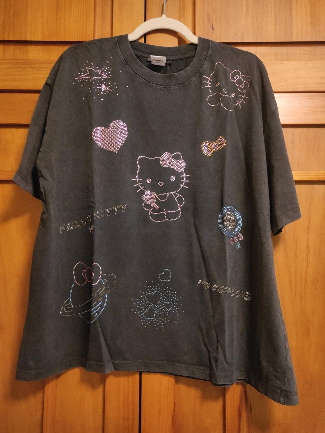 Dark grey T-shirt hanging on wood. It has Hello Kitty rhinestone designs and the text HELLO KITTY and 5 APPLES.