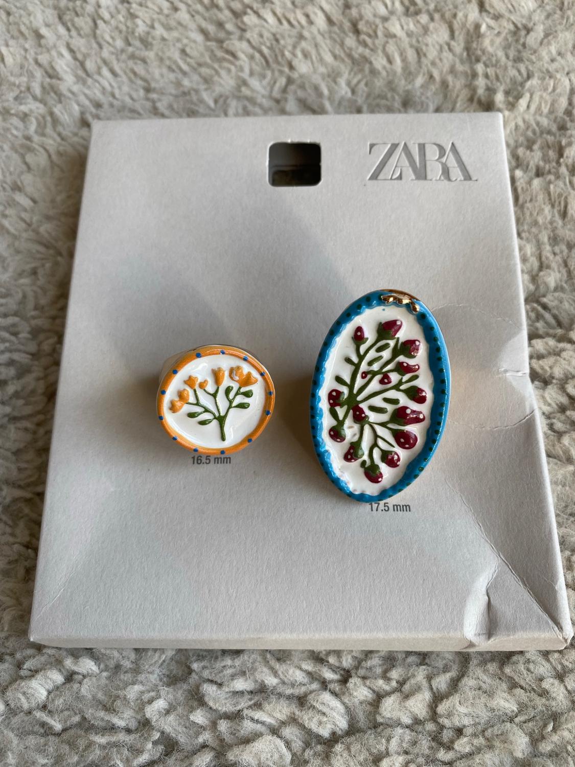 Two rings with a floral design on a white label against a textured background. Text: ZARA, 16.5 mm and 17.5 mm.