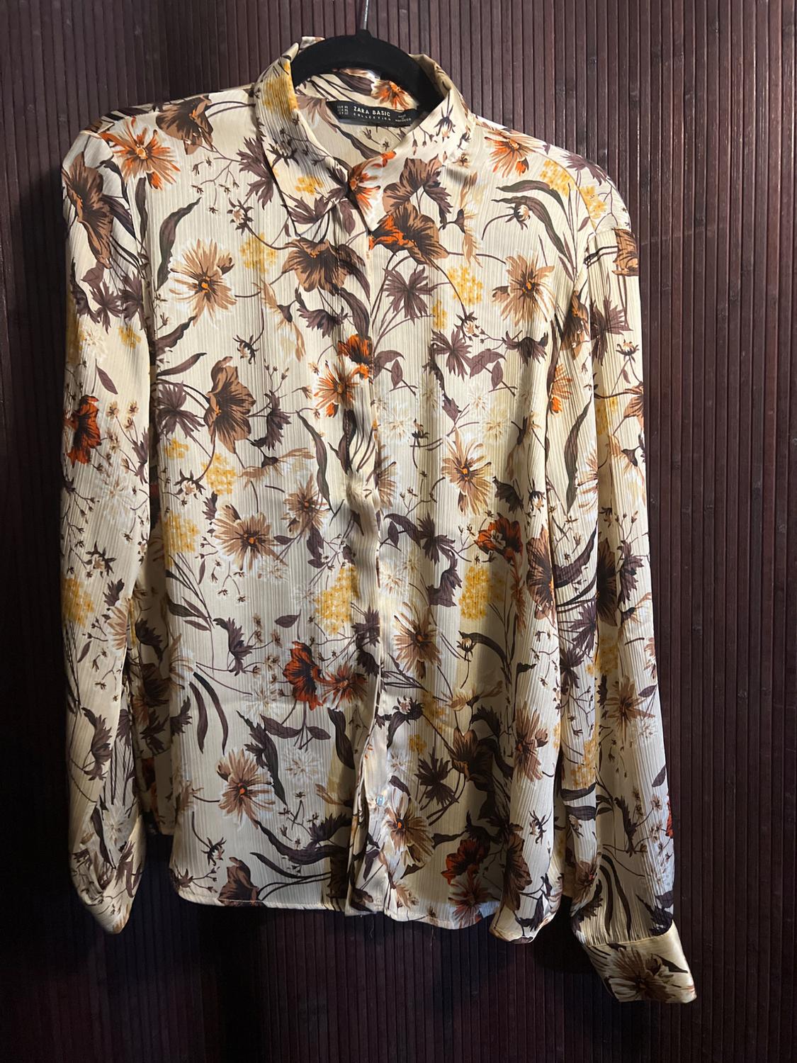 Long-sleeved shirt with a floral print in brown and orange tones, hanging on a hanger against a dark wood background.