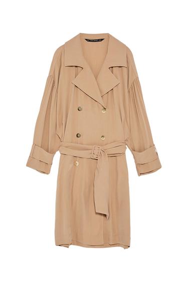 Beige fluid trench coat with double-breasted fastening, belted waist and tab sleeves on a white background. Text: ZARA BASIC.