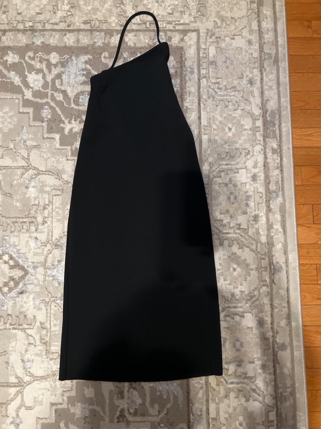 One-shoulder black dress on a beige rug with geometric design and floral details, wooden floor visible in the background.