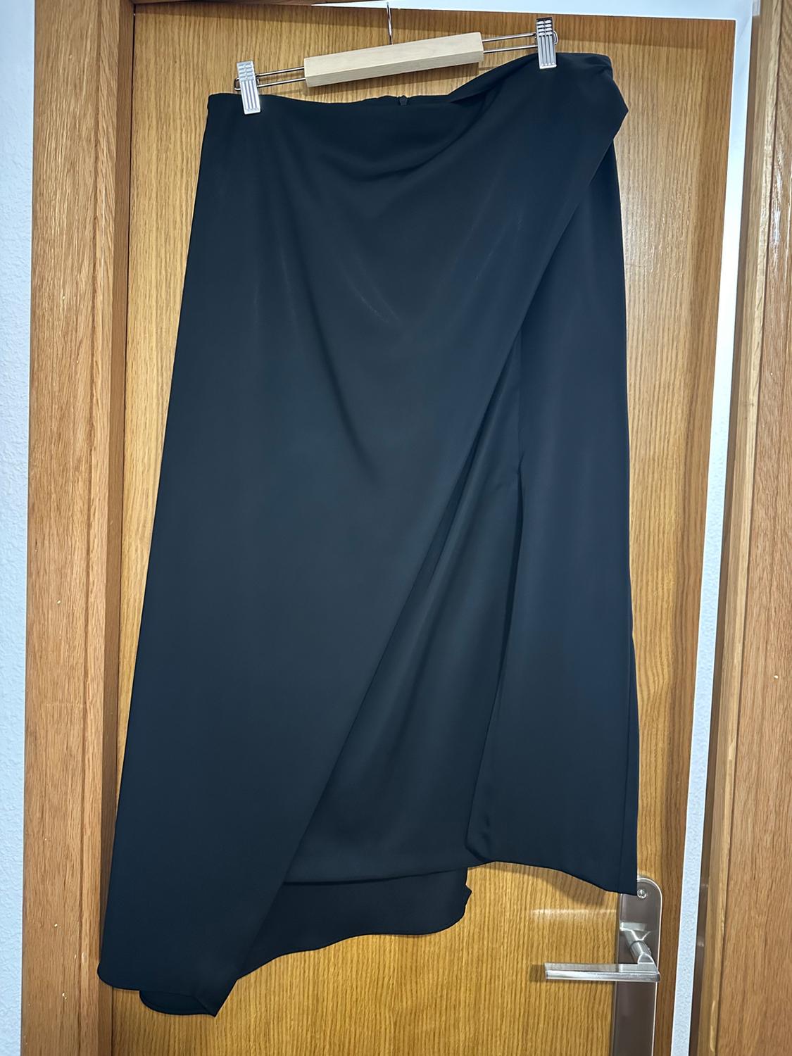 Asymmetrical black skirt hanging on a wooden hanger over a light wooden door.
