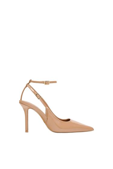 Beige high-heeled shoe with a pointed toe and adjustable ankle strap, on a white background.