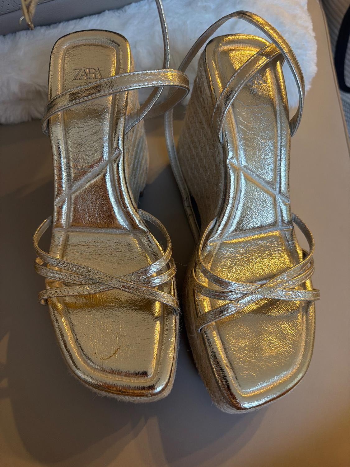 Metallic gold wedge sandals with jute wedges and crossover straps. ZARA text on the insole. Casual-style top view.