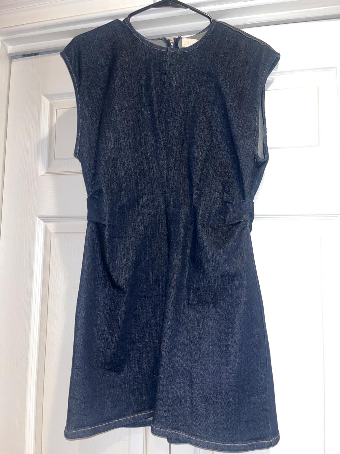 Dark blue, sleeveless denim dress hanging on a hanger in front of a white door.