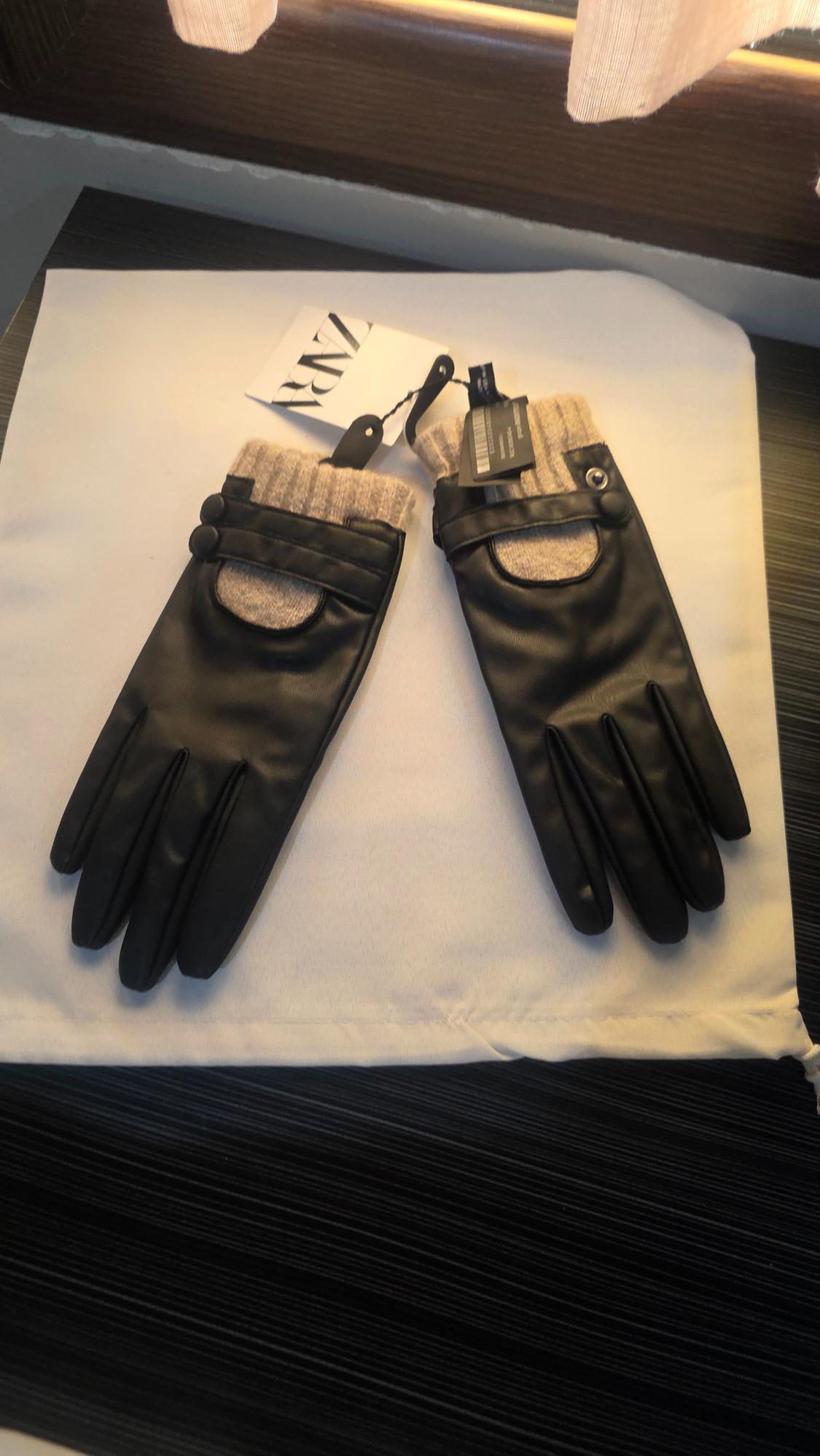 Pair of black gloves with beige knitted cuffs and button detail on a white bag. Label with the text Zara.